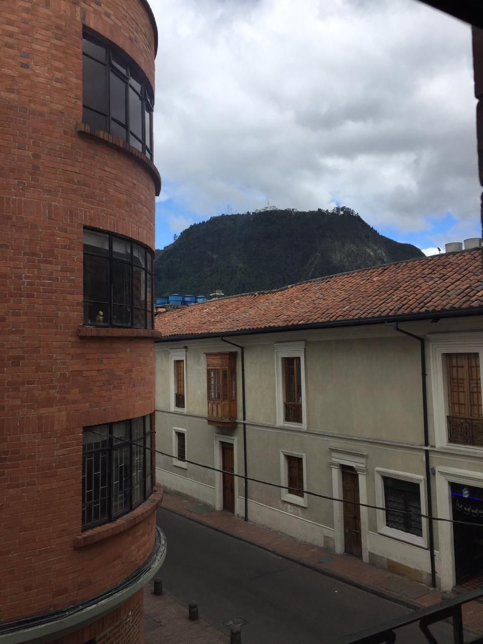 A street view with buildings, a mountain in the background, and a cloudy sky.