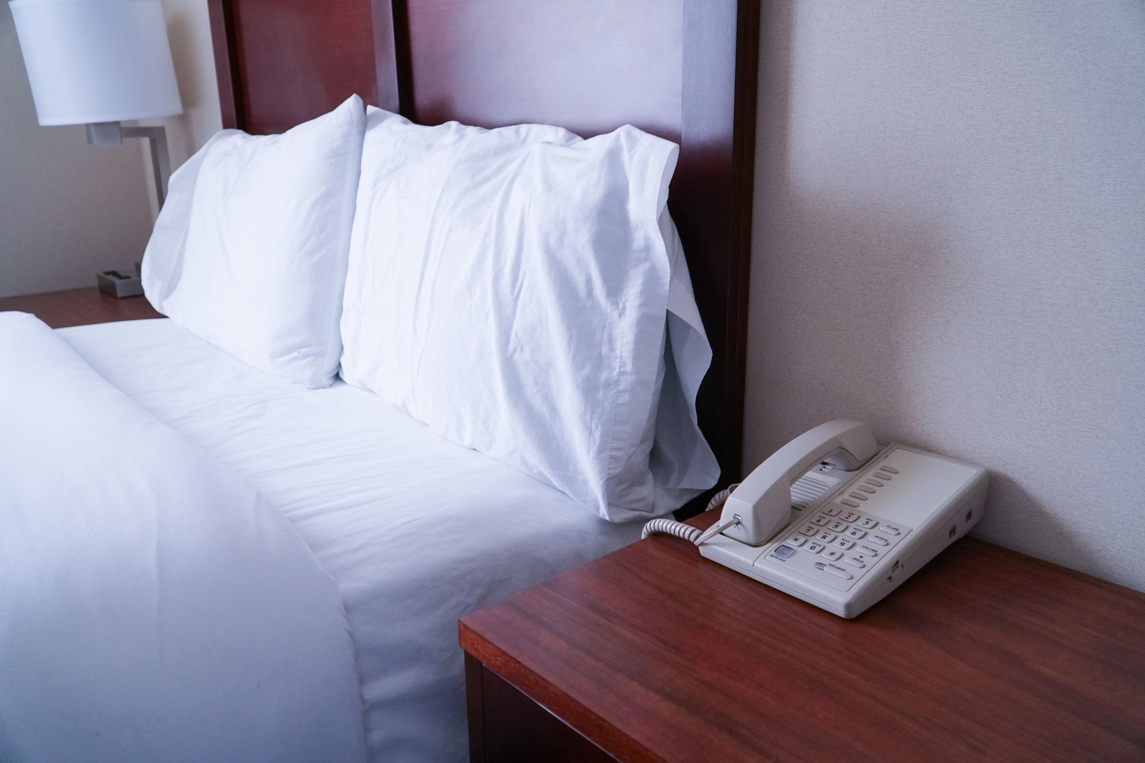 Una habitación de hotel con una cama bien hecha, una mesita de noche con un teléfono y una lámpara.