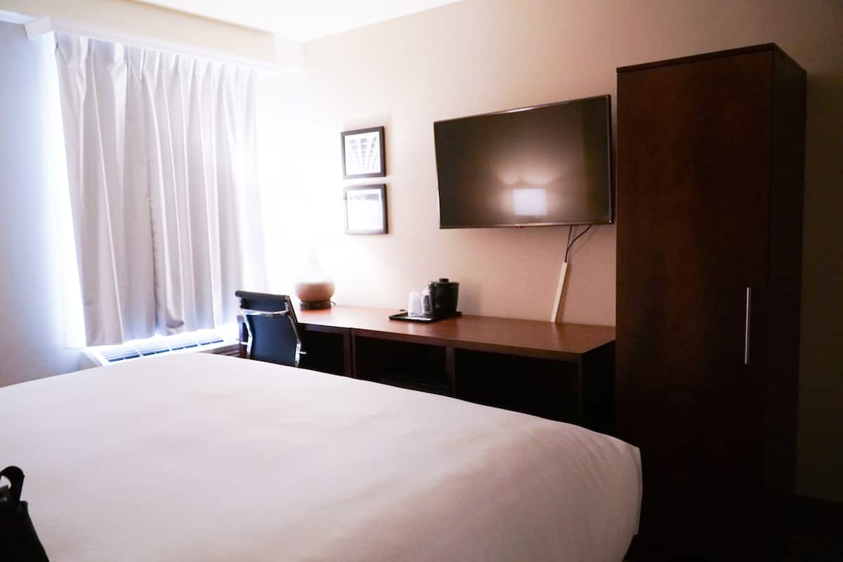 Une chambre d’hôtel avec un grand lit, un bureau doté d’un téléviseur à écran plat, une chaise et une armoire.