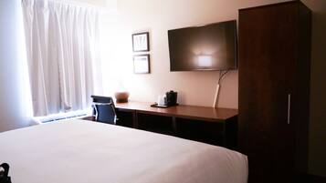 A hotel room with a large bed, a desk with a flat-screen TV, a chair, and a wardrobe.