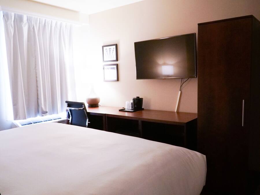 A hotel room with a large bed, a desk with a flat-screen TV, a chair, and a wardrobe.