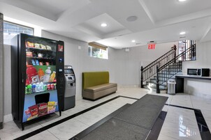 Un moderno hall de entrada con una máquina expendedora, una zona de estar y una escalera que sube a un piso superior.