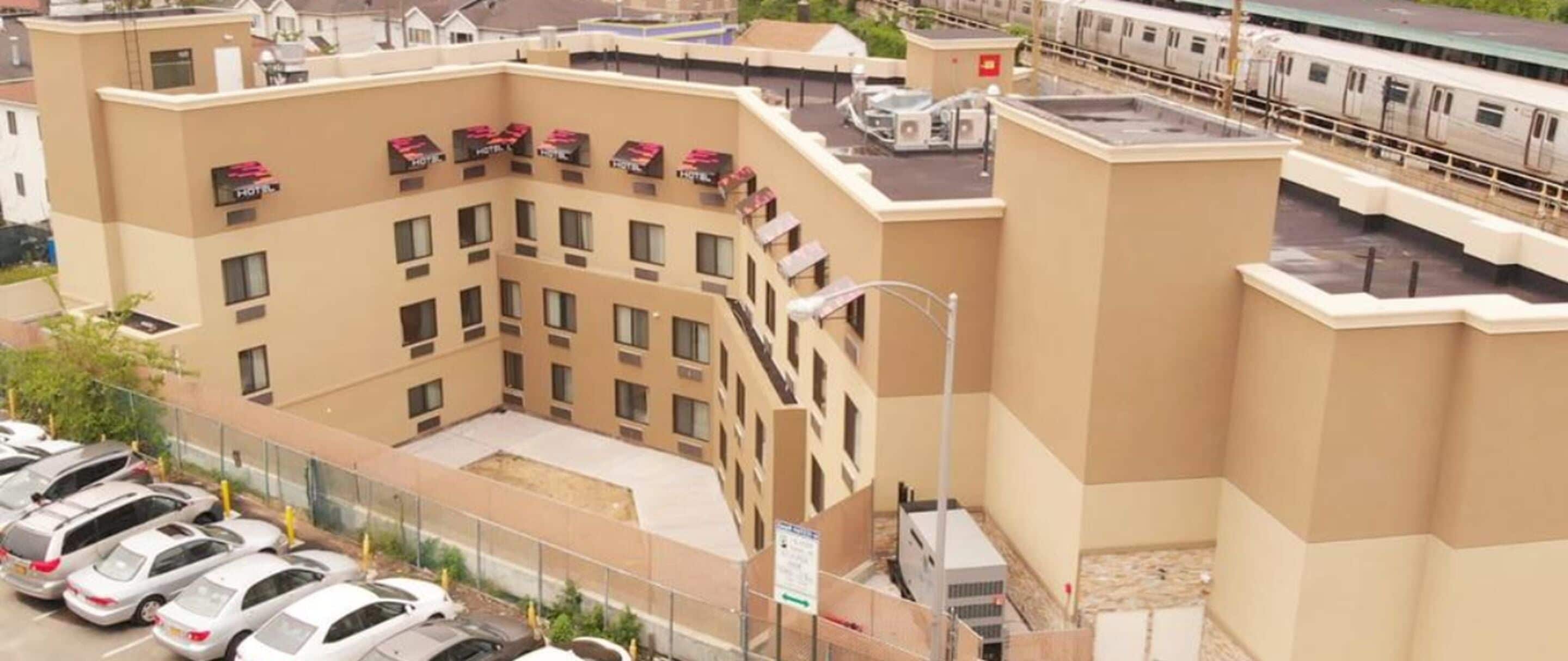 A multi-story hotel with a central courtyard, parking lot, and a train station in the background.