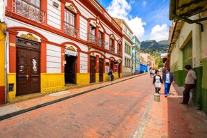 A narrow street with colorful buildings, a clear sky, and a hilly background.
