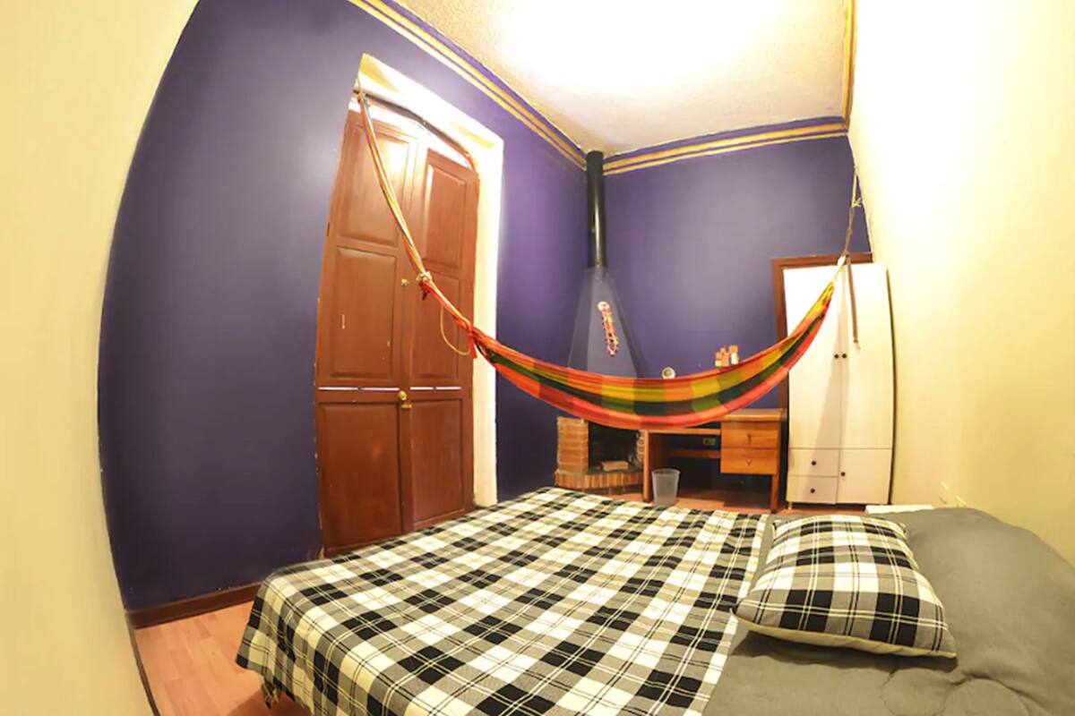 A bedroom with a bed, a hammock, a wardrobe, and a desk.