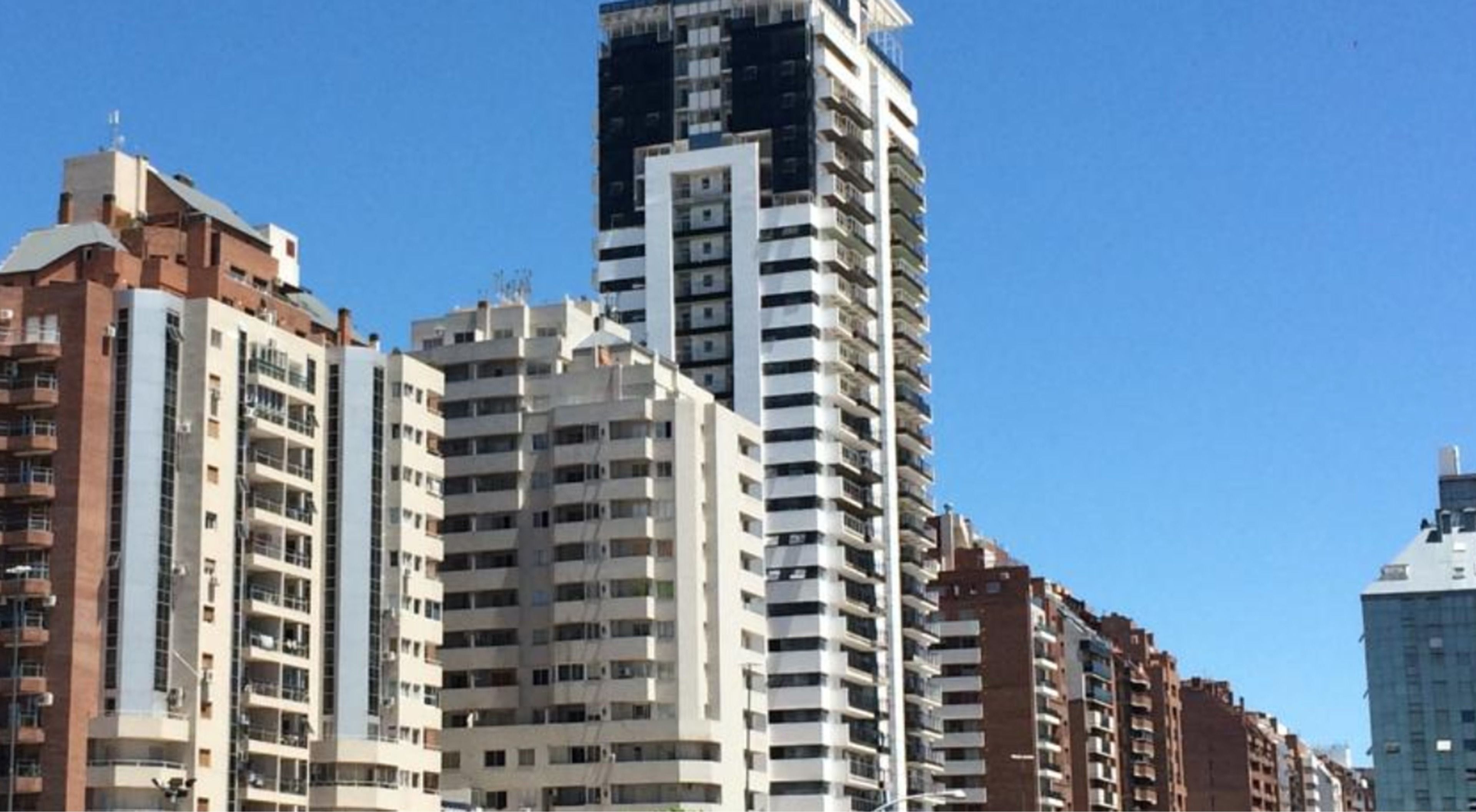 A row of high-rise residential buildings with multiple balconies and a clear blue sky.