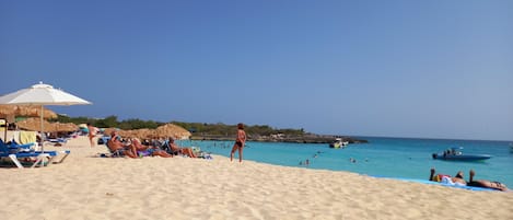 Una playa cerca, arena blanca, sillas reclinables de playa, sombrillas