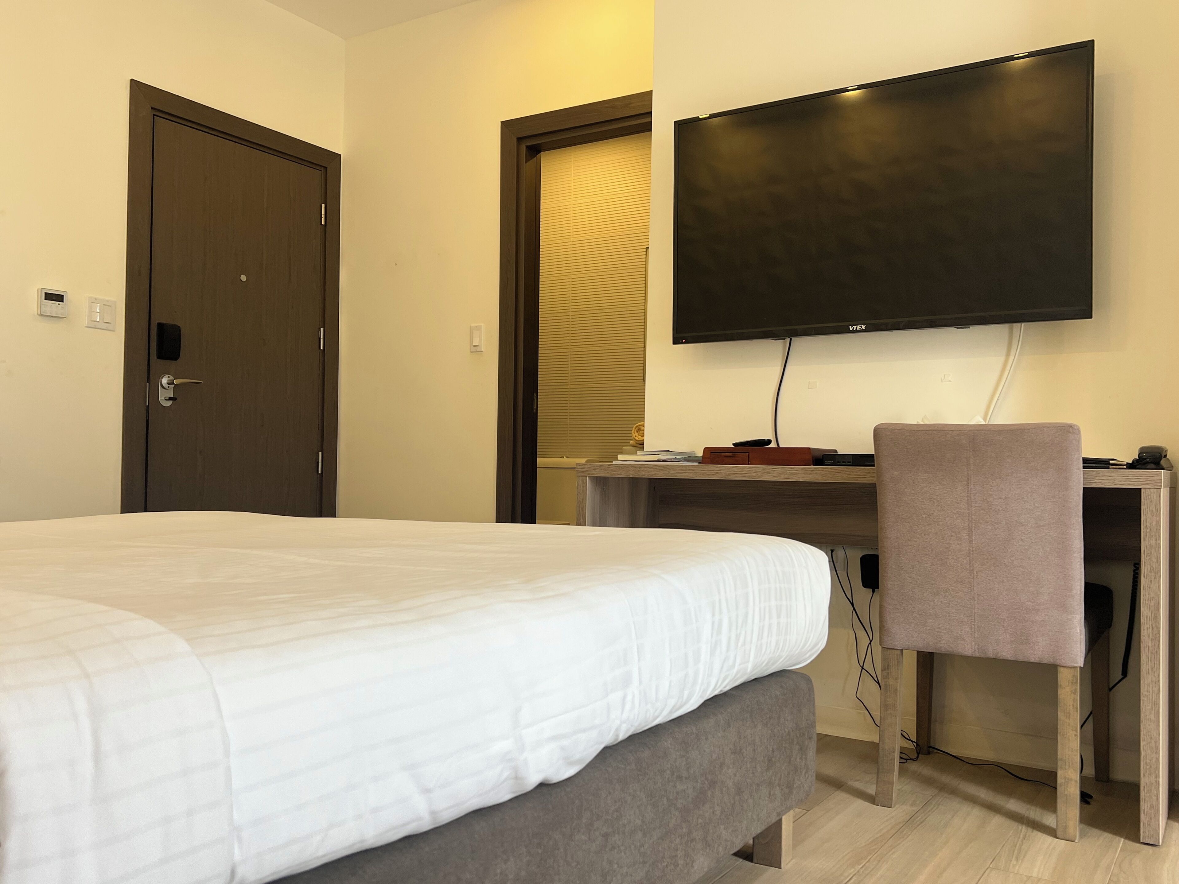 Une chambre d’hôtel avec un lit, un bureau, une chaise, une télévision et une porte.