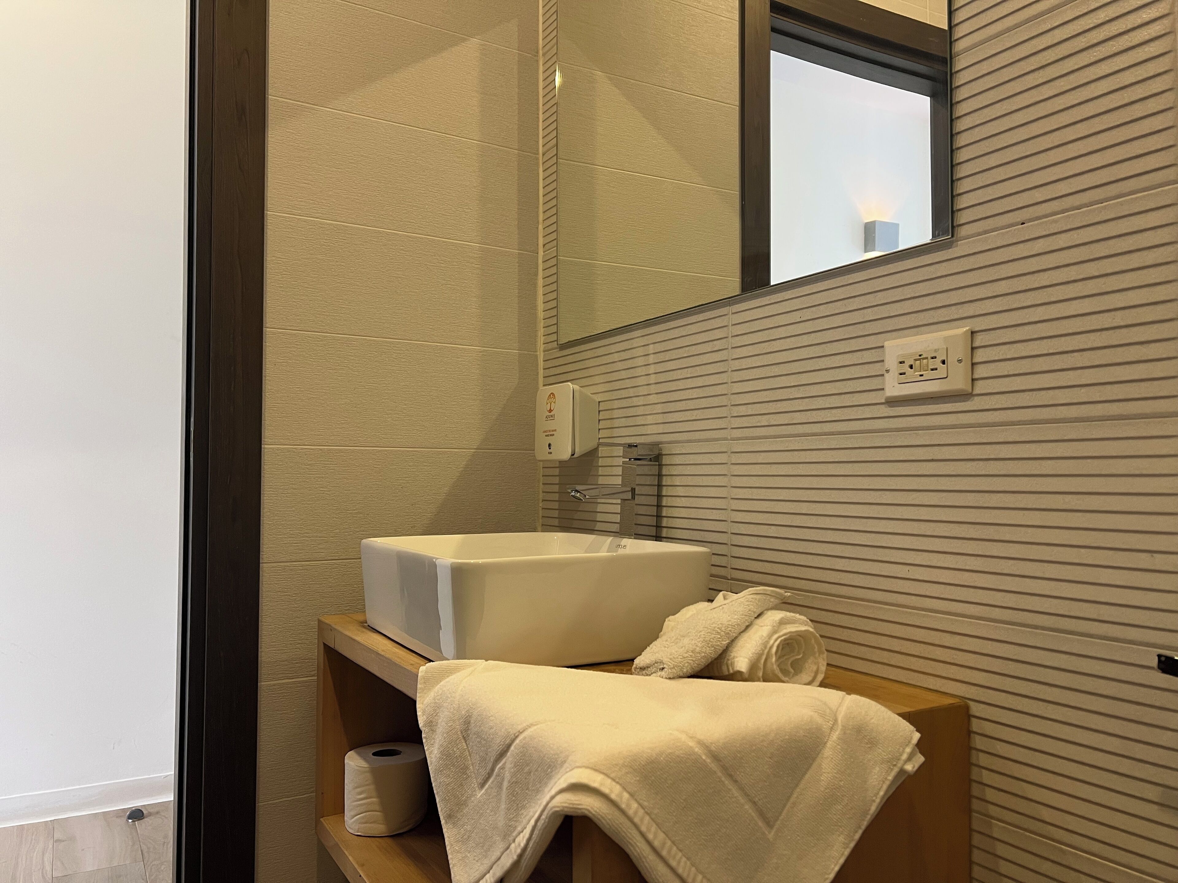 A modern bathroom with a large sink, a mirror, and a towel on a wooden shelf.