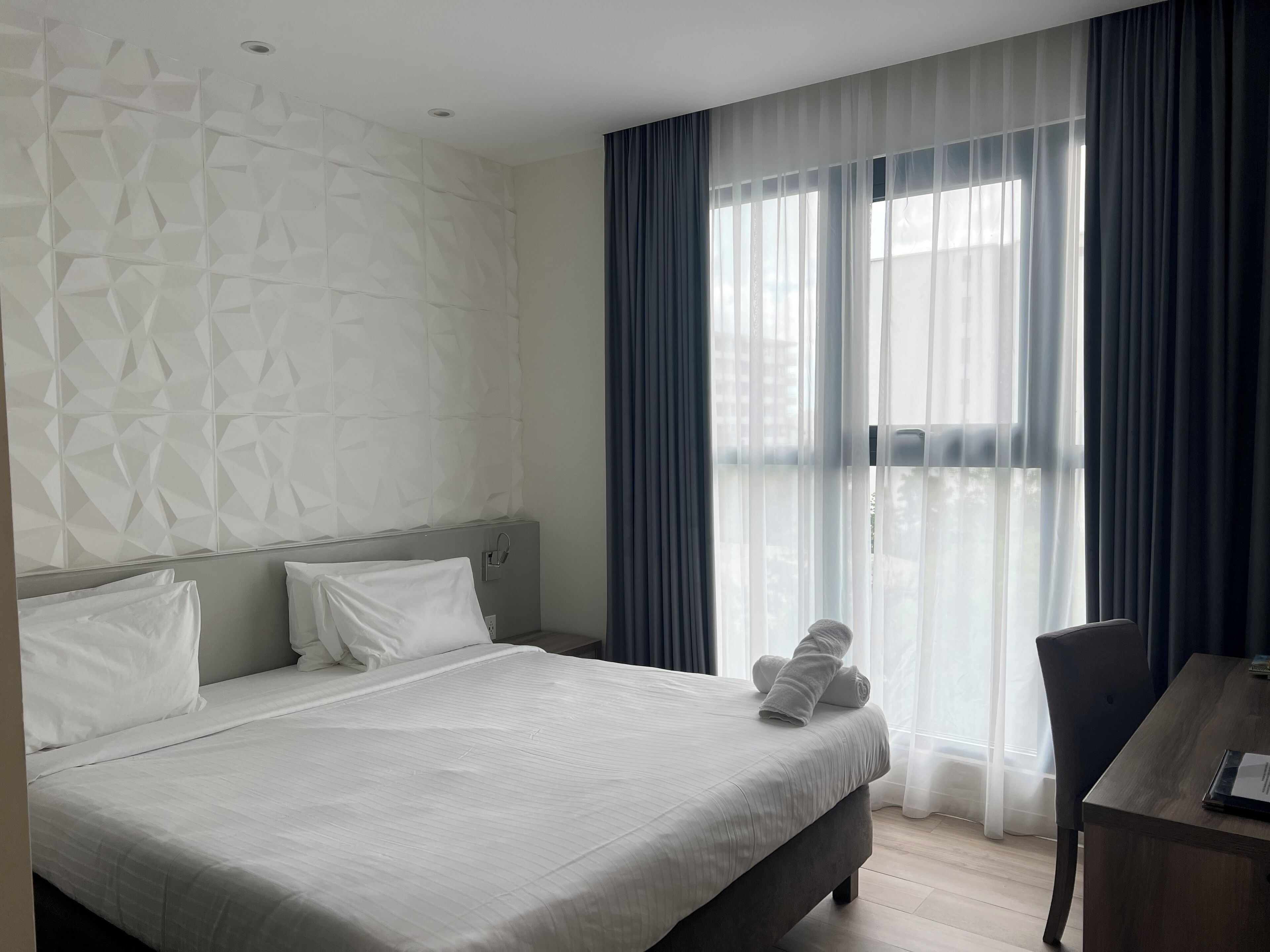 Habitació d'hotel moderna amb un llit gran, un escriptori i vistes a través de cortines translúcides.