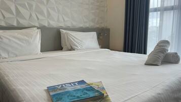 Habitación de hotel con una cama bien hecha, una almohada, una toalla enrollada y un folleto de 'Visit' sobre la cama.