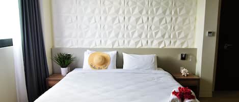 A hotel room with a large bed, a decorative wall, a nightstand with a plant, and a towel with flowers.