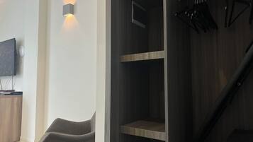 Una habitación moderna con un armario de madera, una silla gris y un televisor montado.