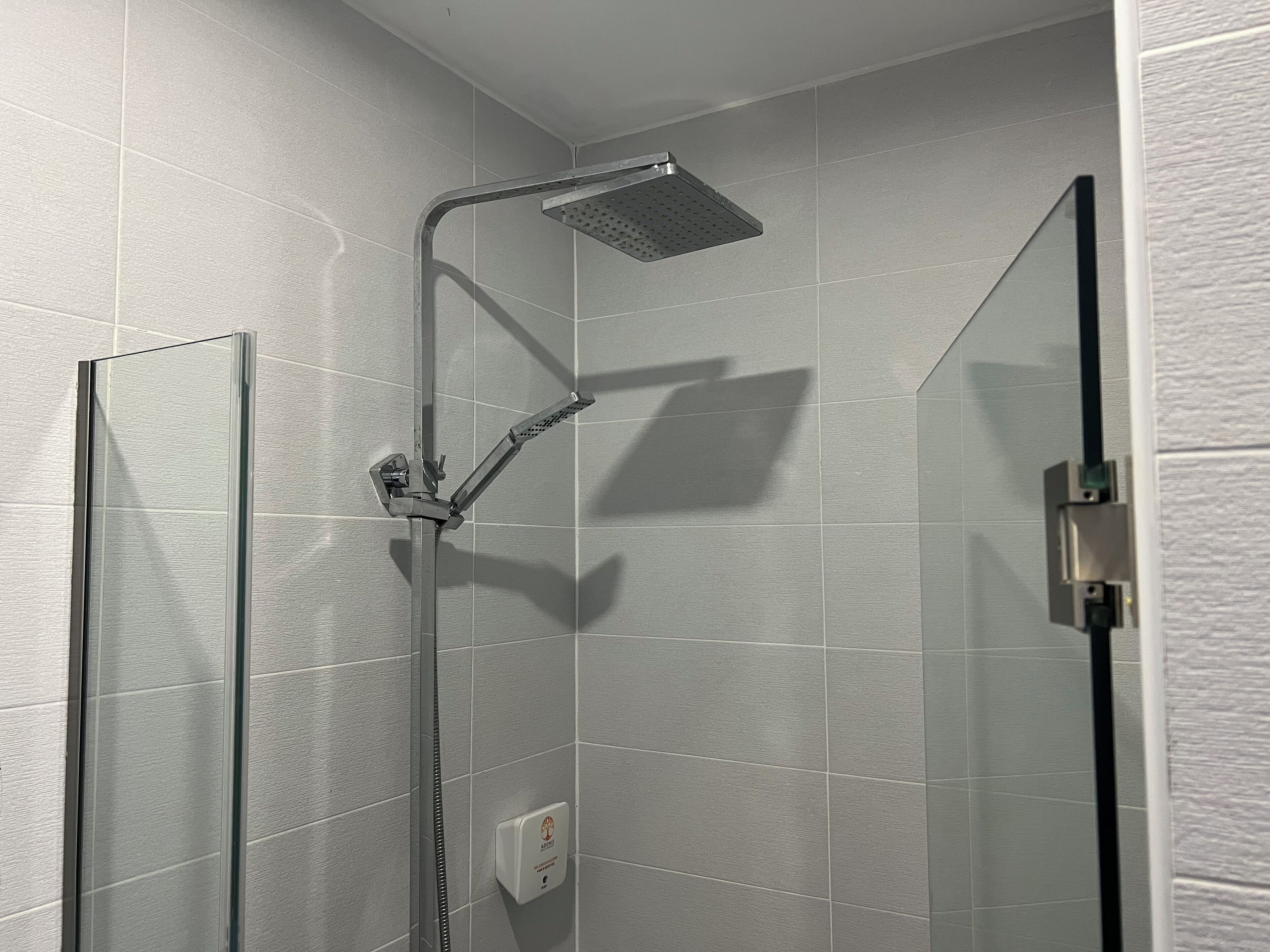 Une douche équipée d’un pommeau de douche à main et d’un panneau de commande fixé au mur.