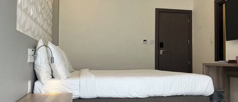Un dormitorio moderno con una cama, una mesita de noche de madera, una lámpara fijada a la pared, una puerta y un televisor en la pared.