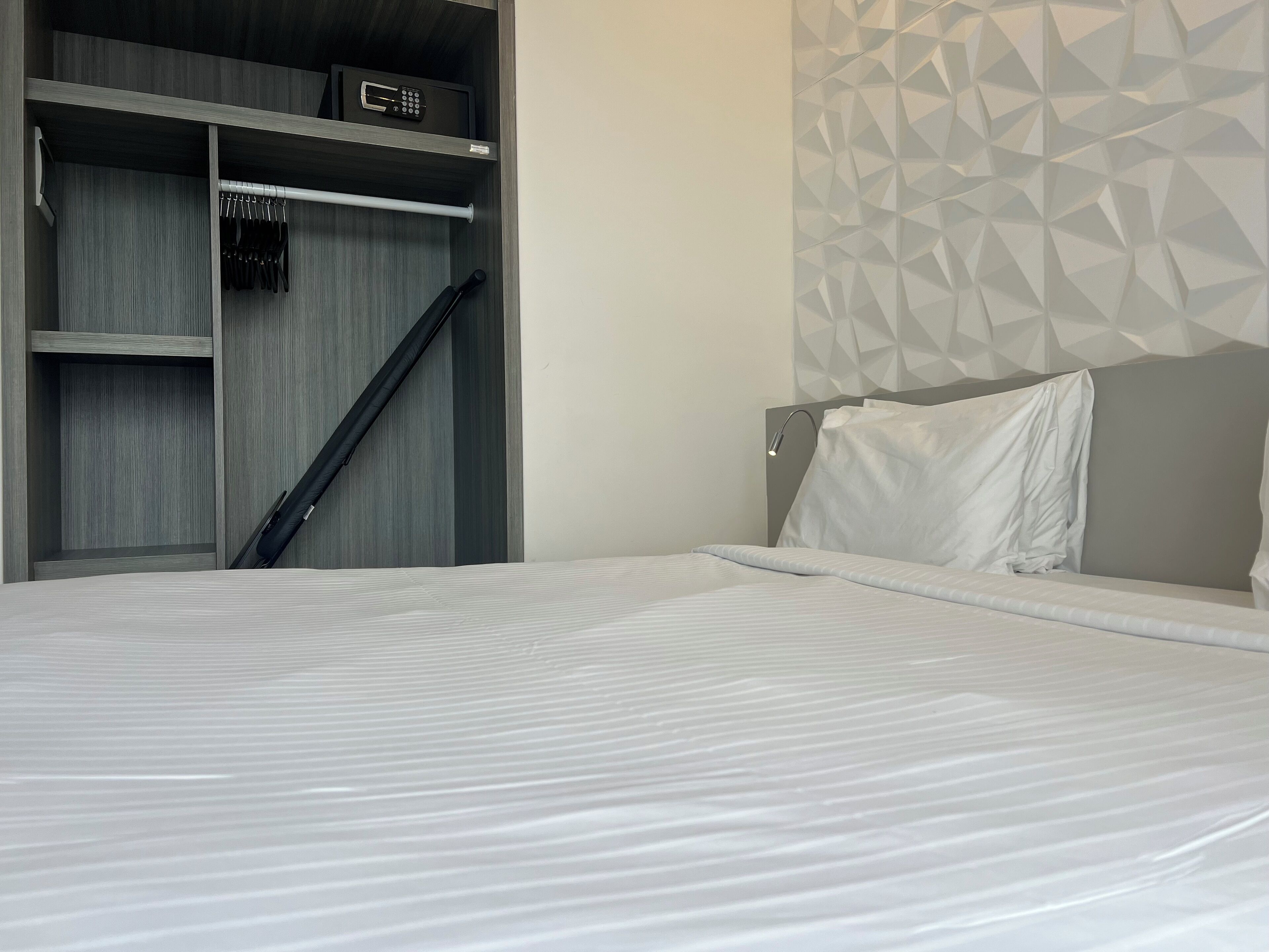 Une chambre d’hôtel moderne avec un lit bien fait, une armoire intégrée avec une serrure et un mur orné d’un motif géométrique.