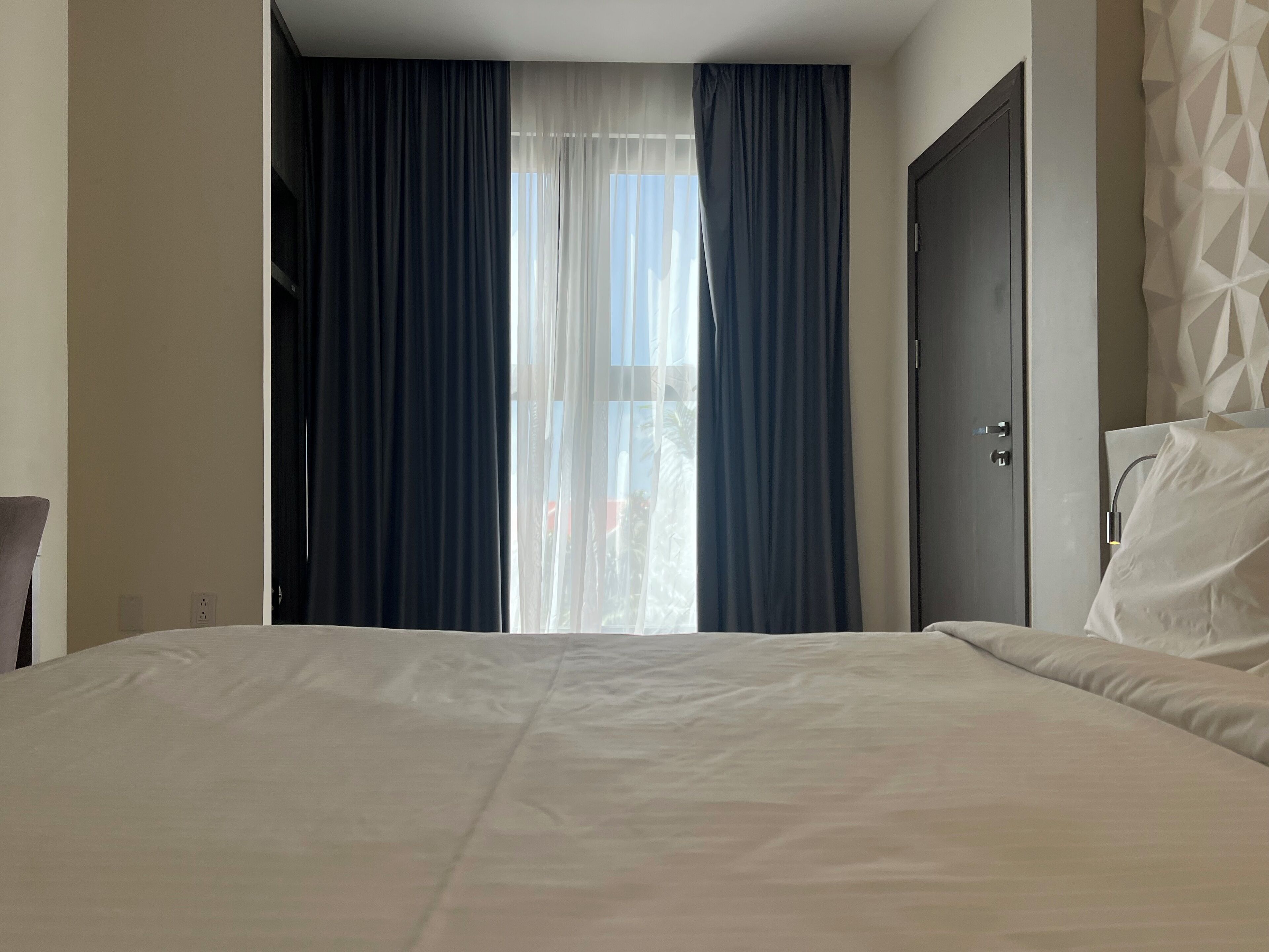 A hotel room with a bed, a door, and a window with curtains.