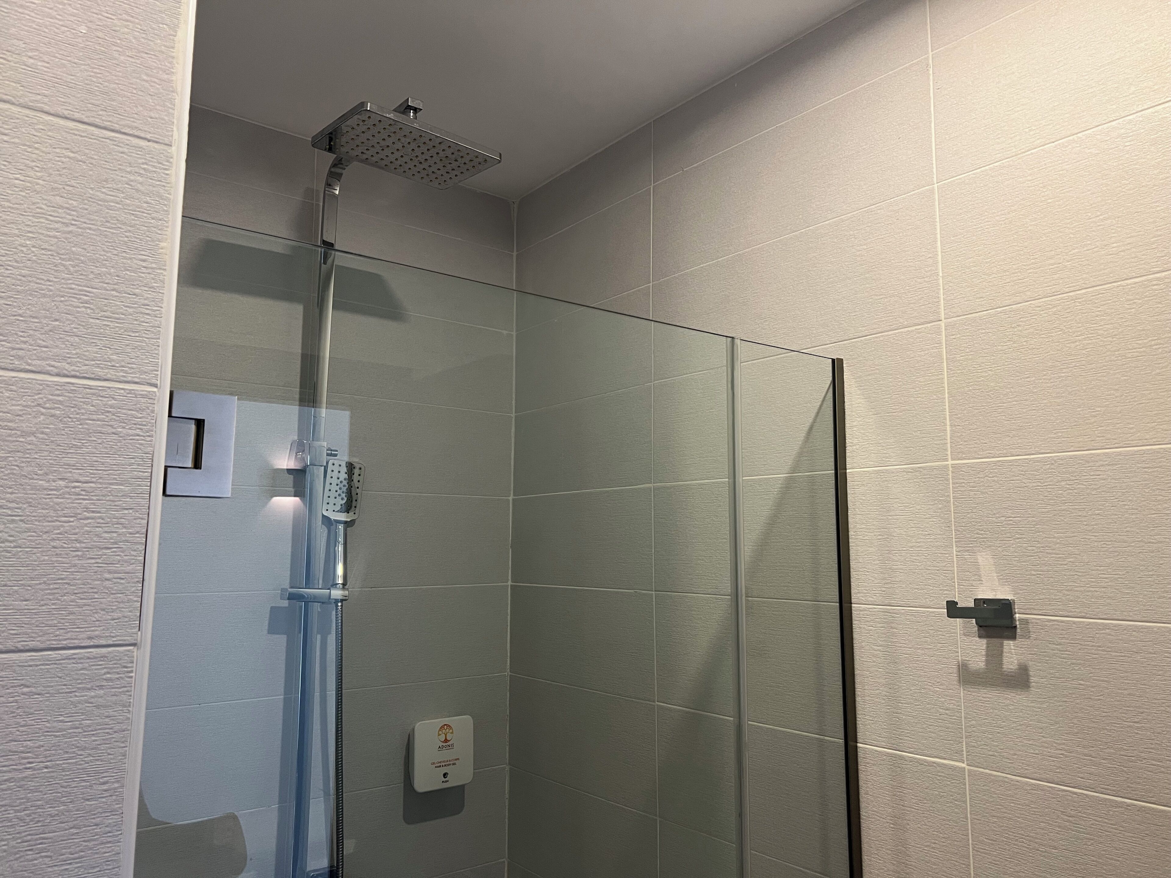 A glass-enclosed shower with a handheld showerhead and a control panel.