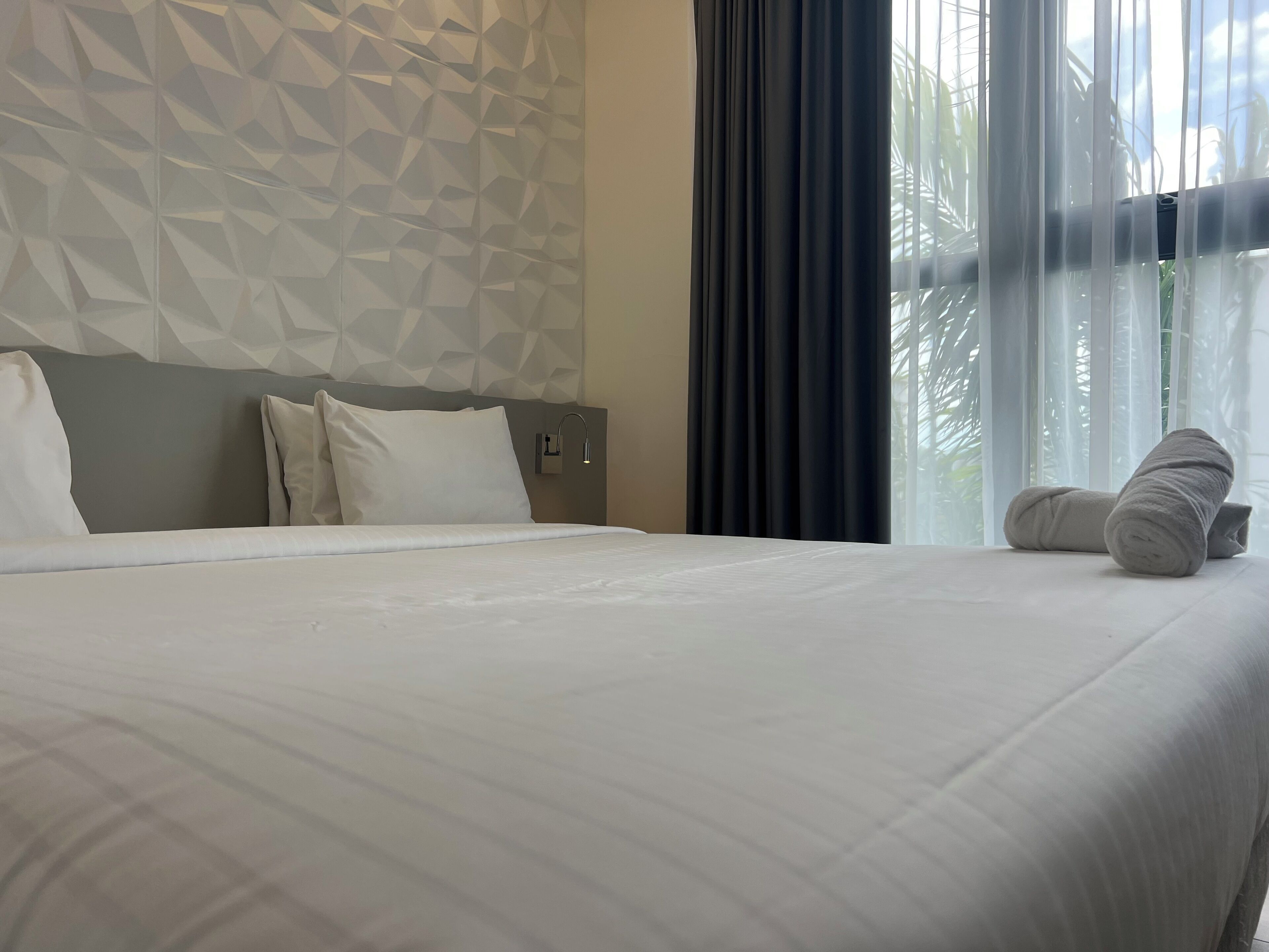 Una cama bien hecha con sábanas blancas, cabecera gris y pared con estampado geométrico.