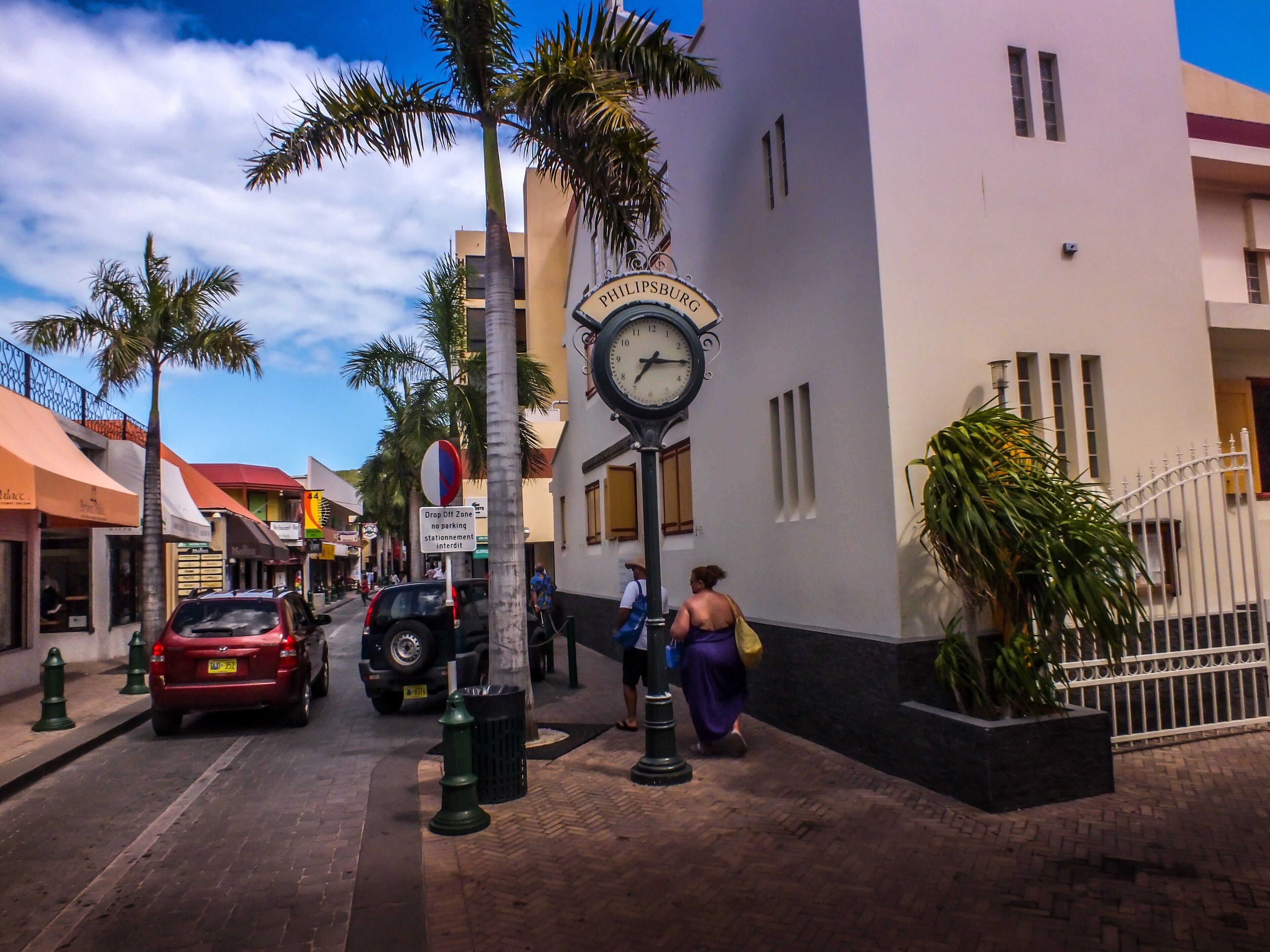 Una calle con un reloj, palmeras y edificios.