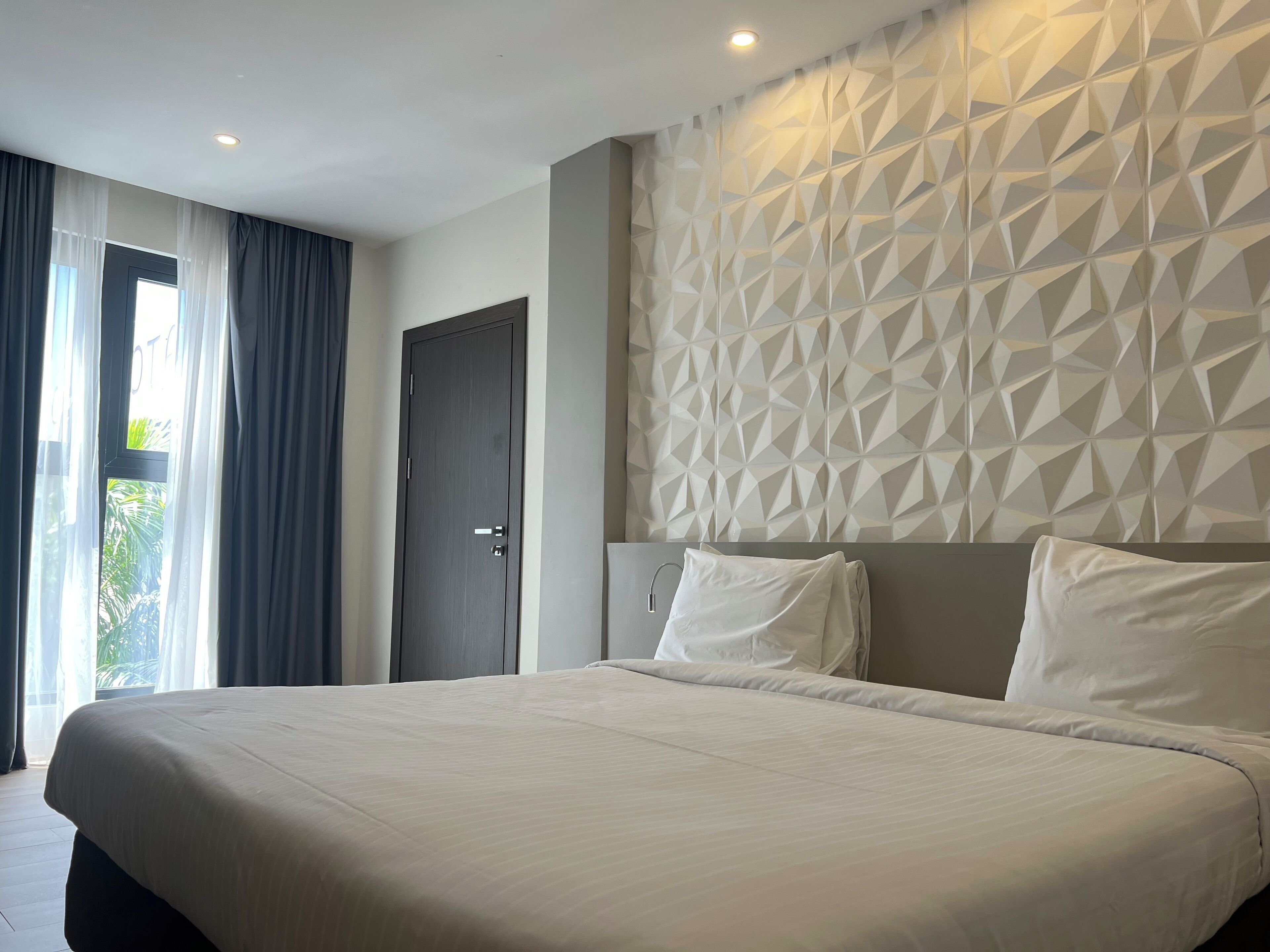 Quarto de hotel moderno com uma cama grande, parede com padrão geométrico e porta que dá para uma varanda.