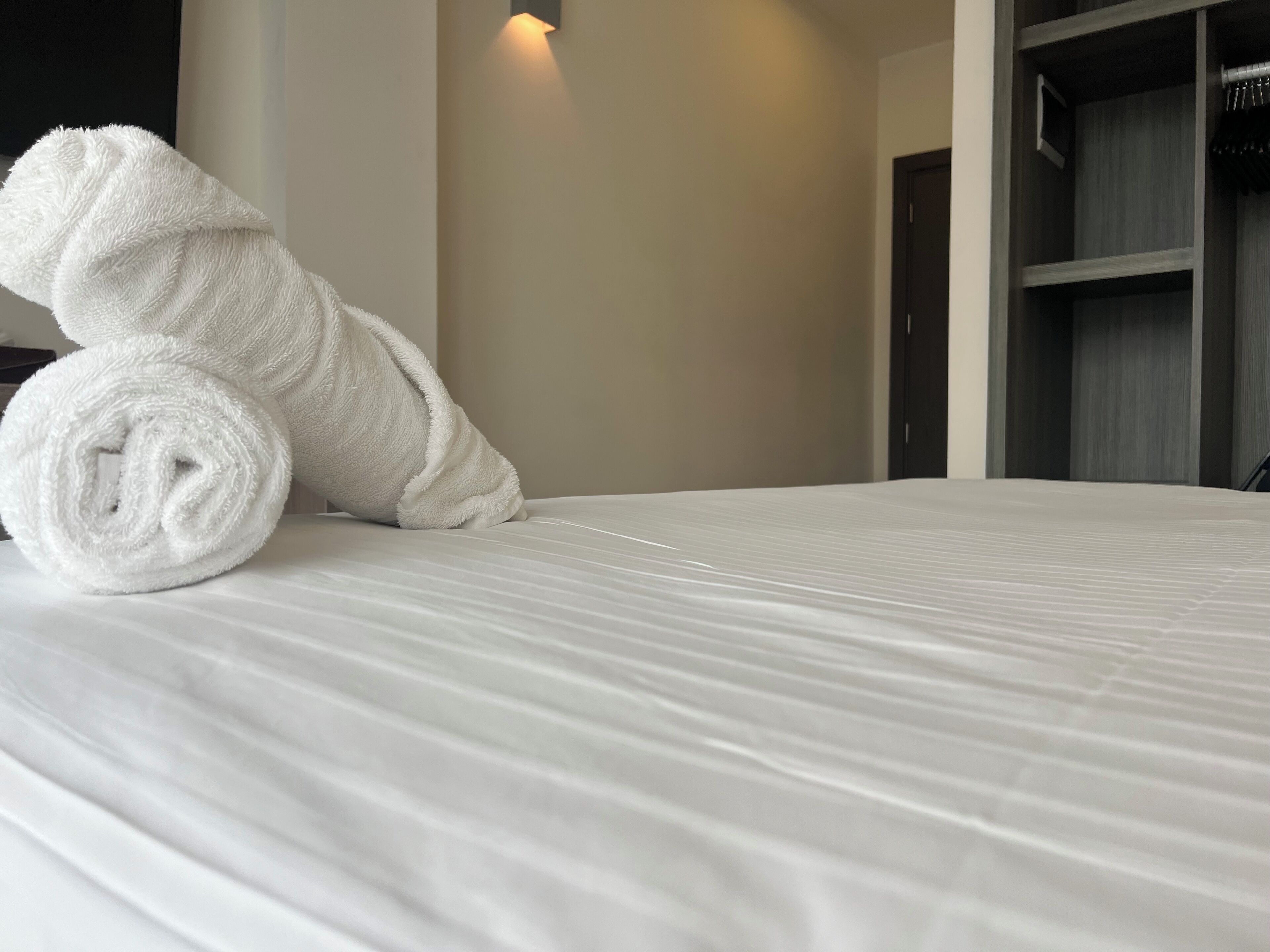 A neatly made bed with a rolled white towel on it.