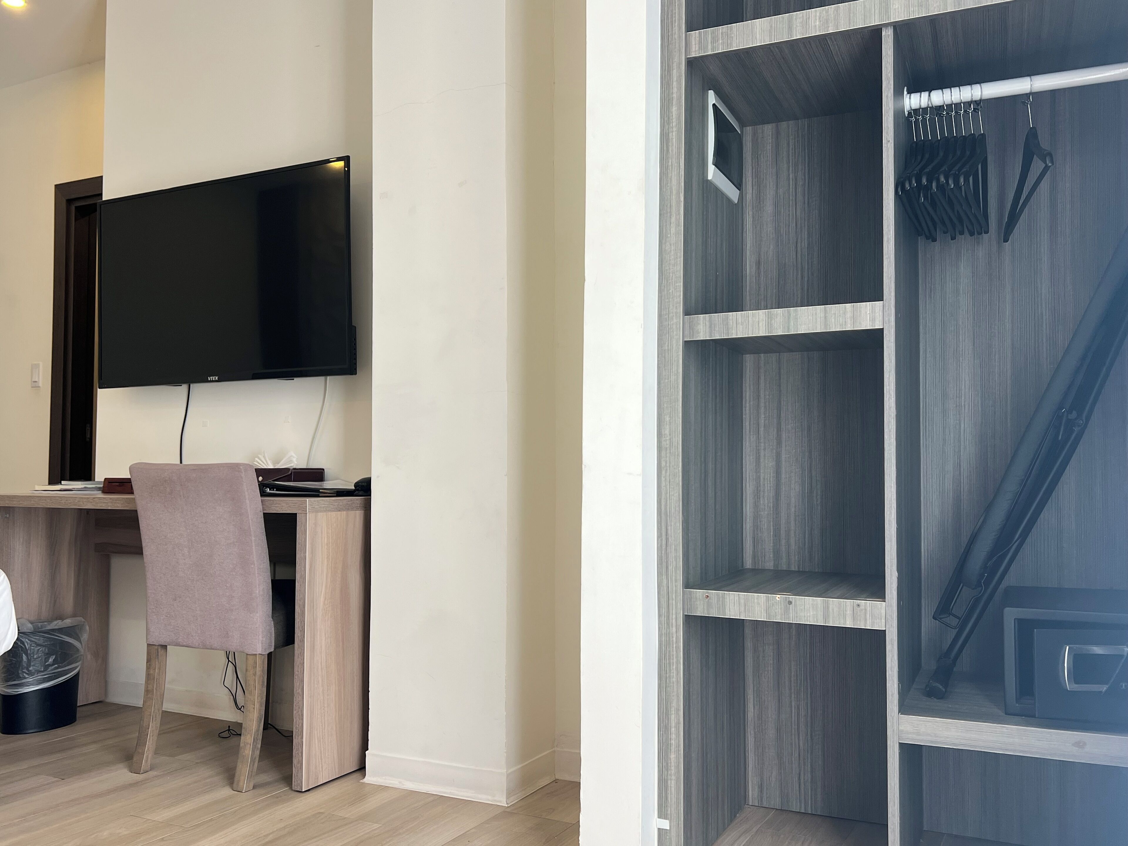 A modern room with a flat-screen TV, a desk with a chair, and a wardrobe with a hanging rack.