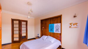 A bedroom with a bed, wooden floor, a wardrobe, a desk with a chair, a map on the wall, and a ceiling light. - La Quinta - Hostel (Bogotá)