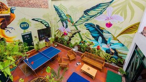 An indoor recreational area with a ping pong table, seating, and a mural with tropical plants and a bird. - La Quinta - Hostel (Bogotá)