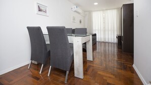 Ein Essbereich mit einem Glastisch und vier grauen Stühlen, einer weißen Wand mit zwei gerahmten Bildern und einem Holzboden.