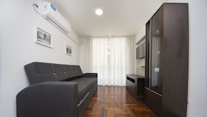 Ein modernes Wohnzimmer mit einem grauen Sofa, einer dunkelholznen Kommode und einem Flachbildfernseher.