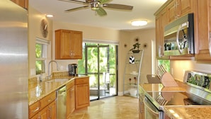 A modern kitchen with granite countertops, stainless steel appliances, wooden cabinets, and a ceiling fan. - 601 Lewis Court (Marco Island)