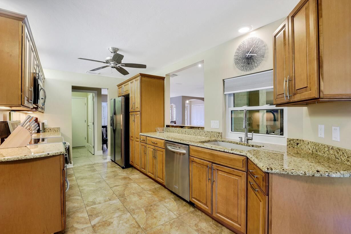 A modern kitchen with wooden cabinets, granite countertops, a built-in dishwasher, and a ceiling fan.