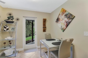 A dining area with a table and chairs, a shelf with decorative items, and a door leading to a garden. - 601 Lewis Court (Marco Island)