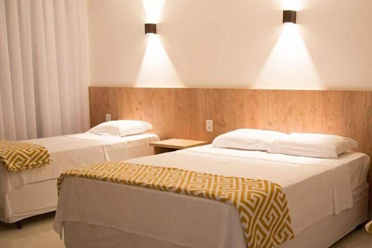 A hotel room with two single beds, each with a patterned throw blanket, a wooden headboard, and wall-mounted lighting.