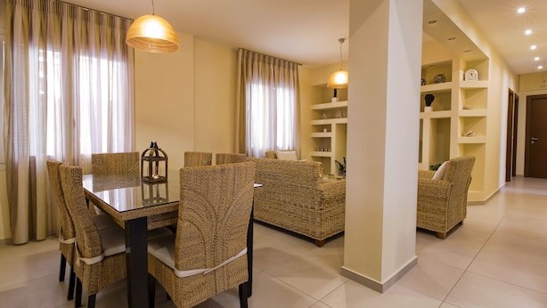 A dining area with a glass table and wicker chairs, a living area with a sofa, and a hallway with shelves. - Cashel House (Corfu)