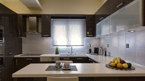 A modern kitchen with dark cabinetry, a white countertop, and a dining area with a table set for two. - Cashel House (Corfu)