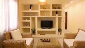 A living room with wicker furniture, a flat-screen TV, and shelves with decorative items. - Cashel House (Corfu)