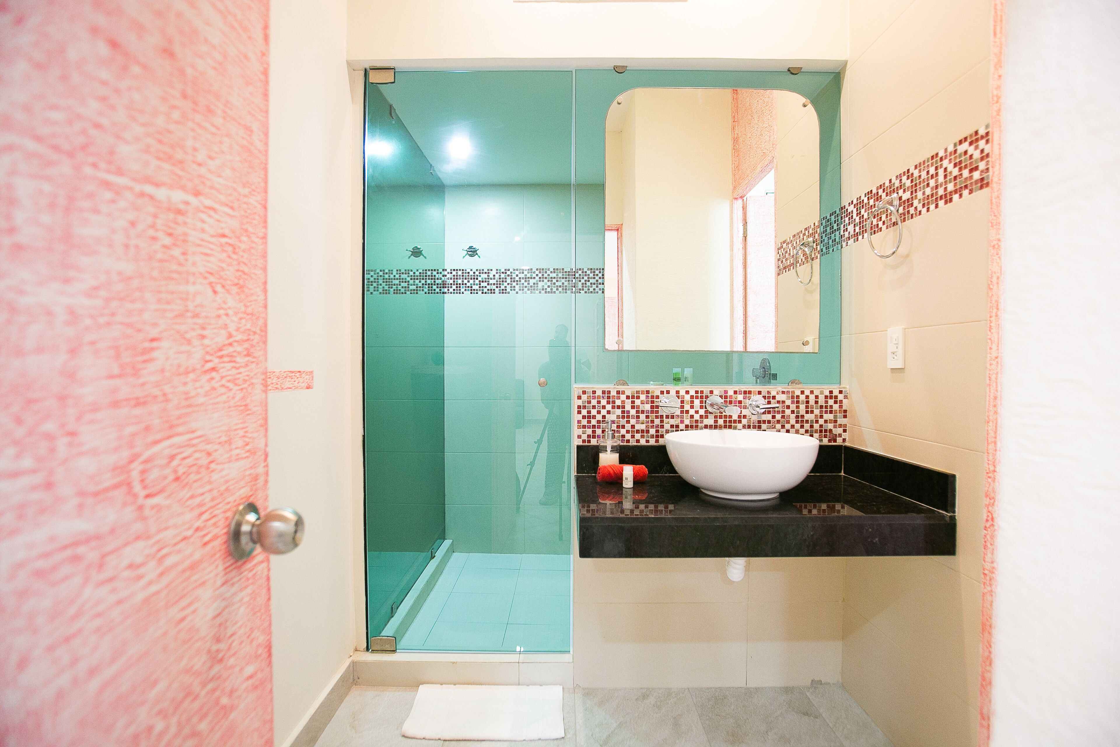 Un bagno con cabina doccia in vetro, lavabo bianco e schienale rivestito di piastrelle.