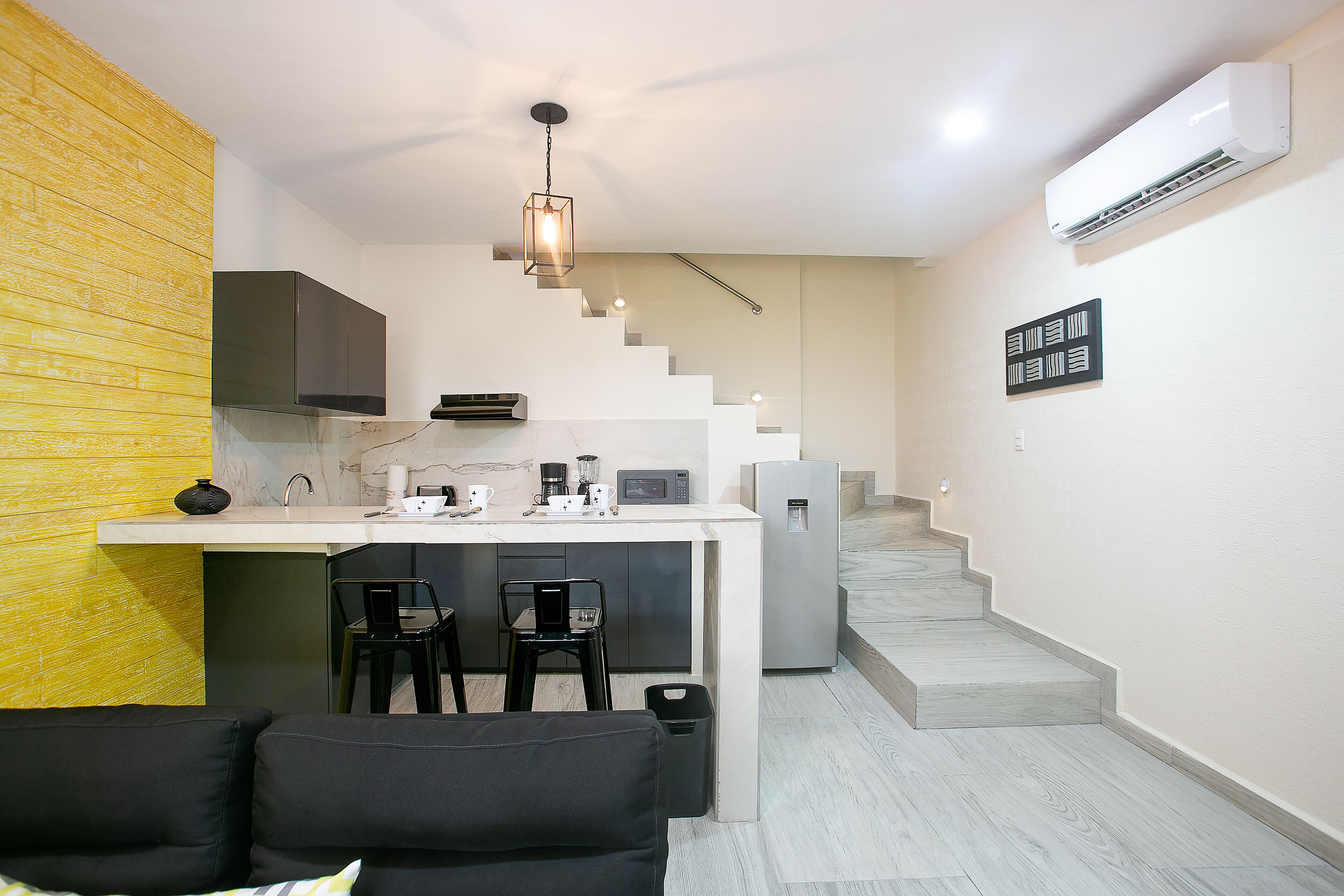 A compact living space with a kitchen area, a dining table with chairs, a staircase, and a sofa.