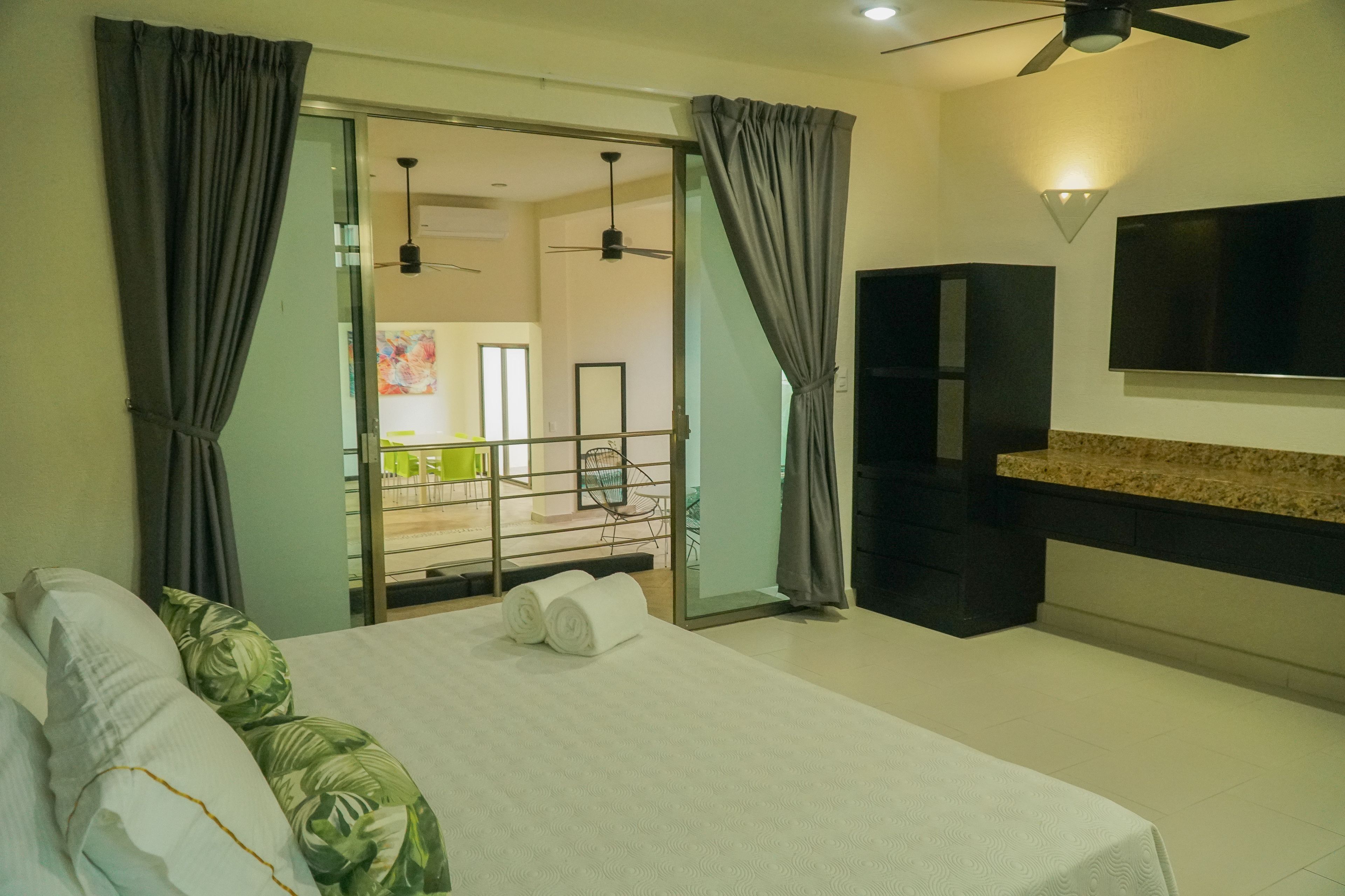 A hotel room with a bed, curtains, a TV, and a balcony.