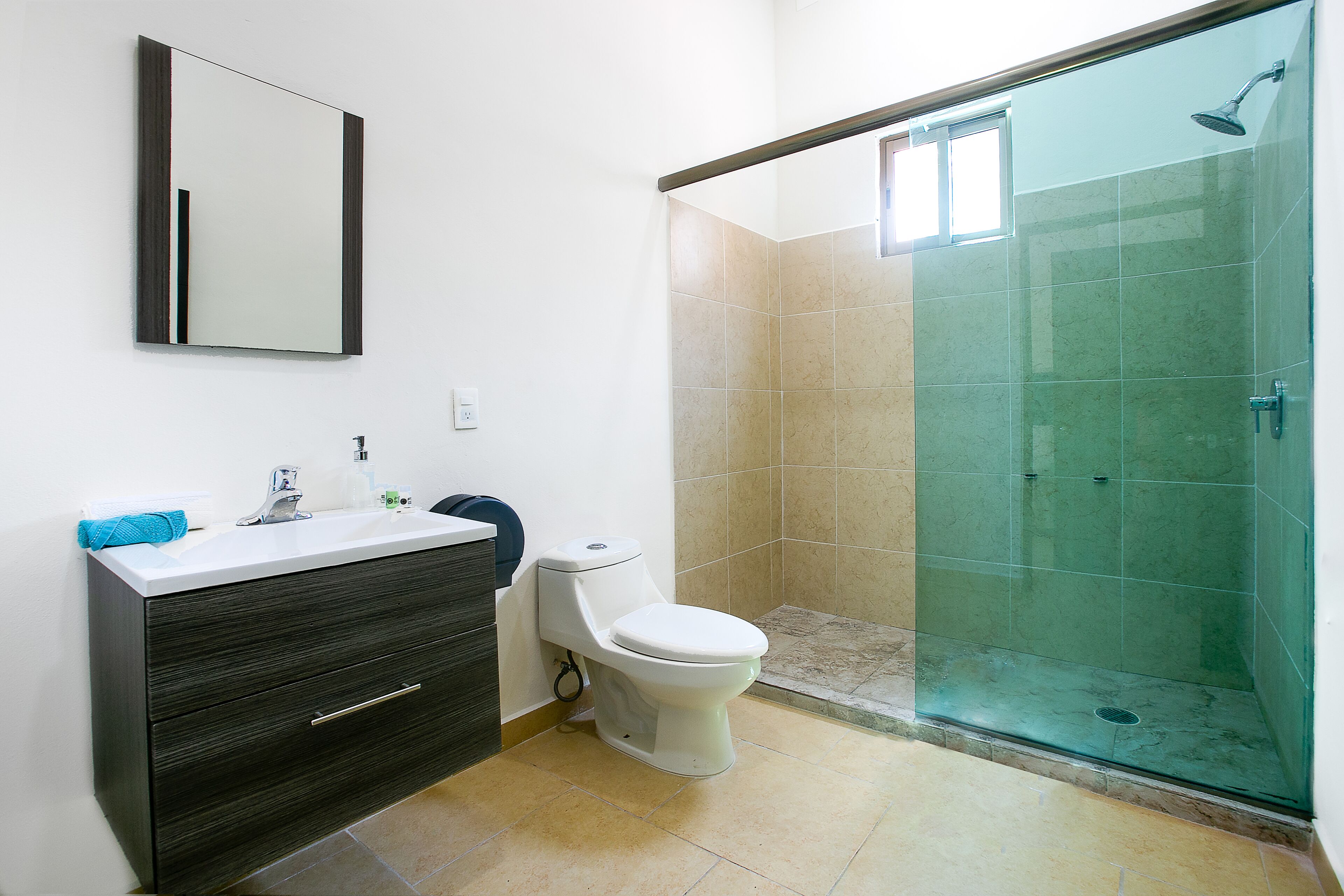 Un baño con inodoro, lavamanos y ducha con mampara de vidrio.
