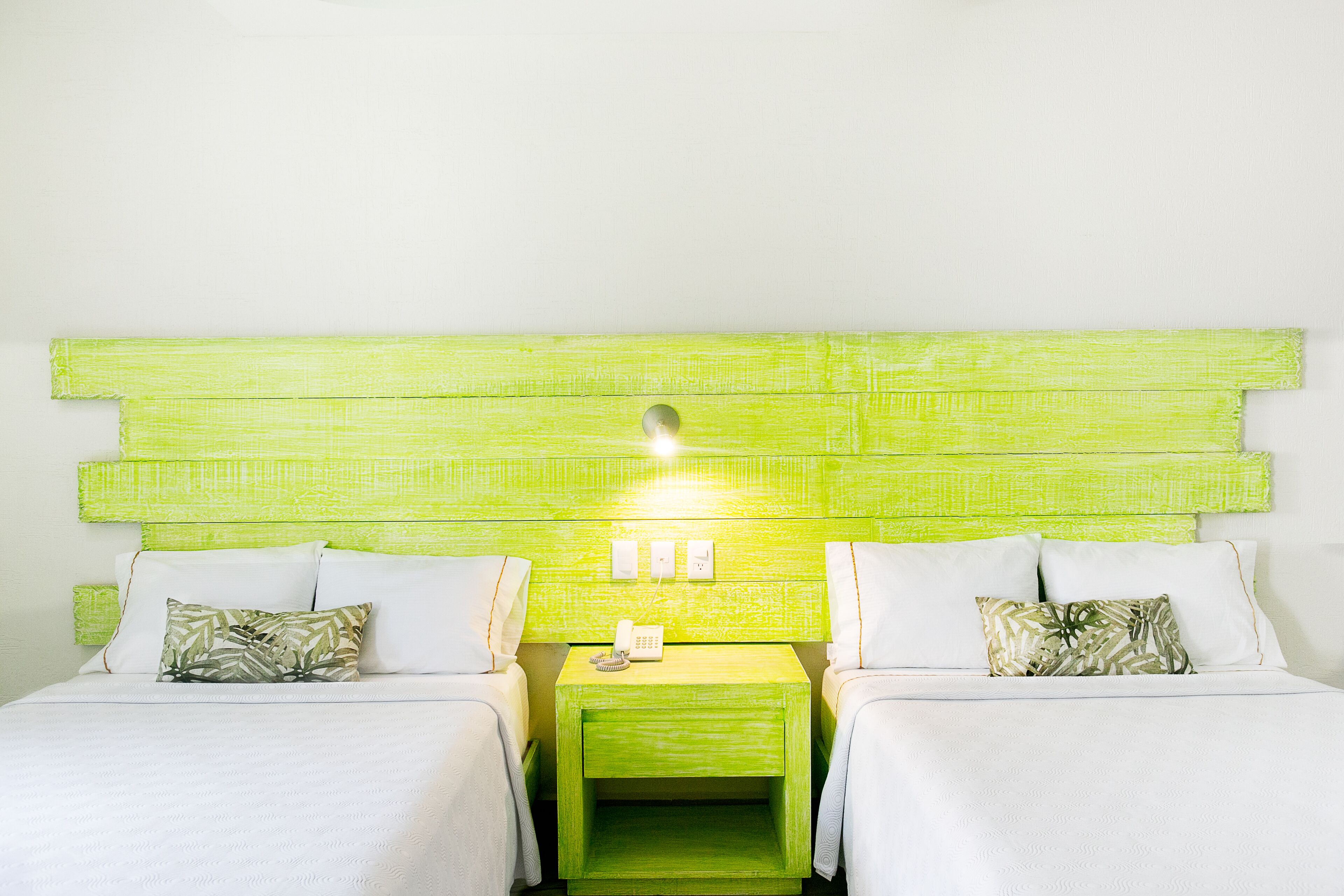 A room with two beds, a green nightstand with a phone, and a green headboard.