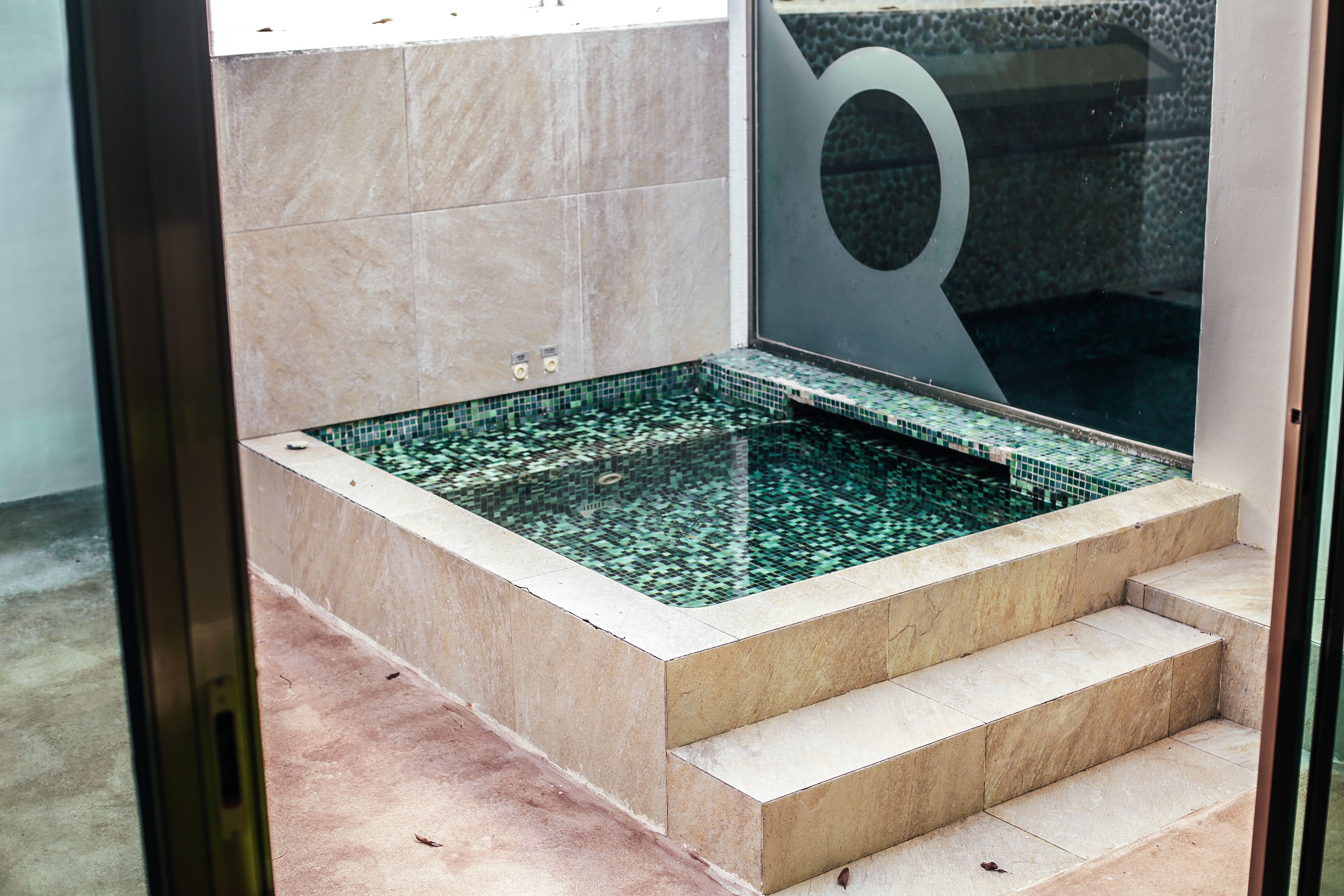 A spa area with a rectangular hot tub, tiled walls, and a glass door with a circular design.