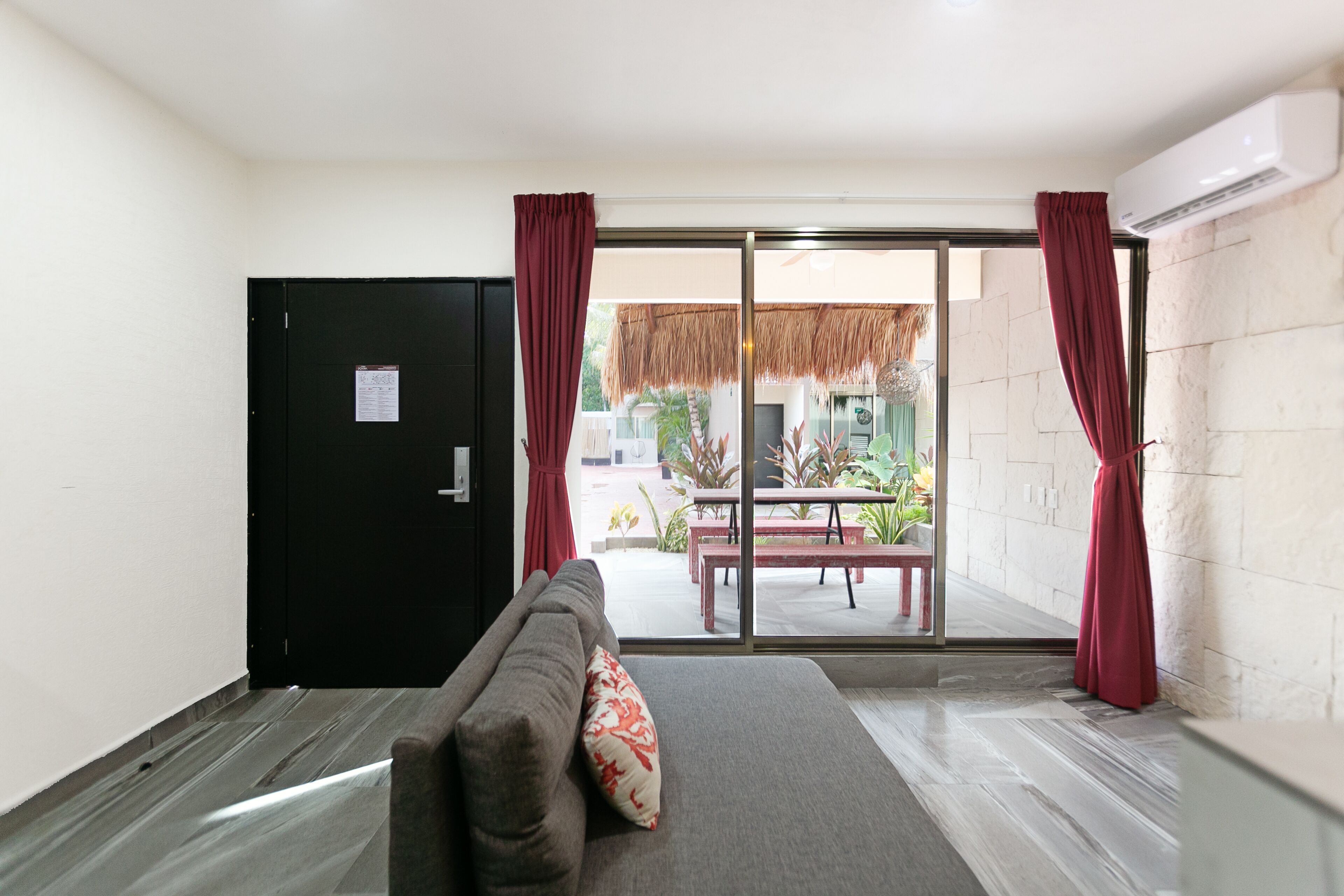 A room with a sofa, a sliding glass door leading to an outdoor area with a table and chairs, and a black door.