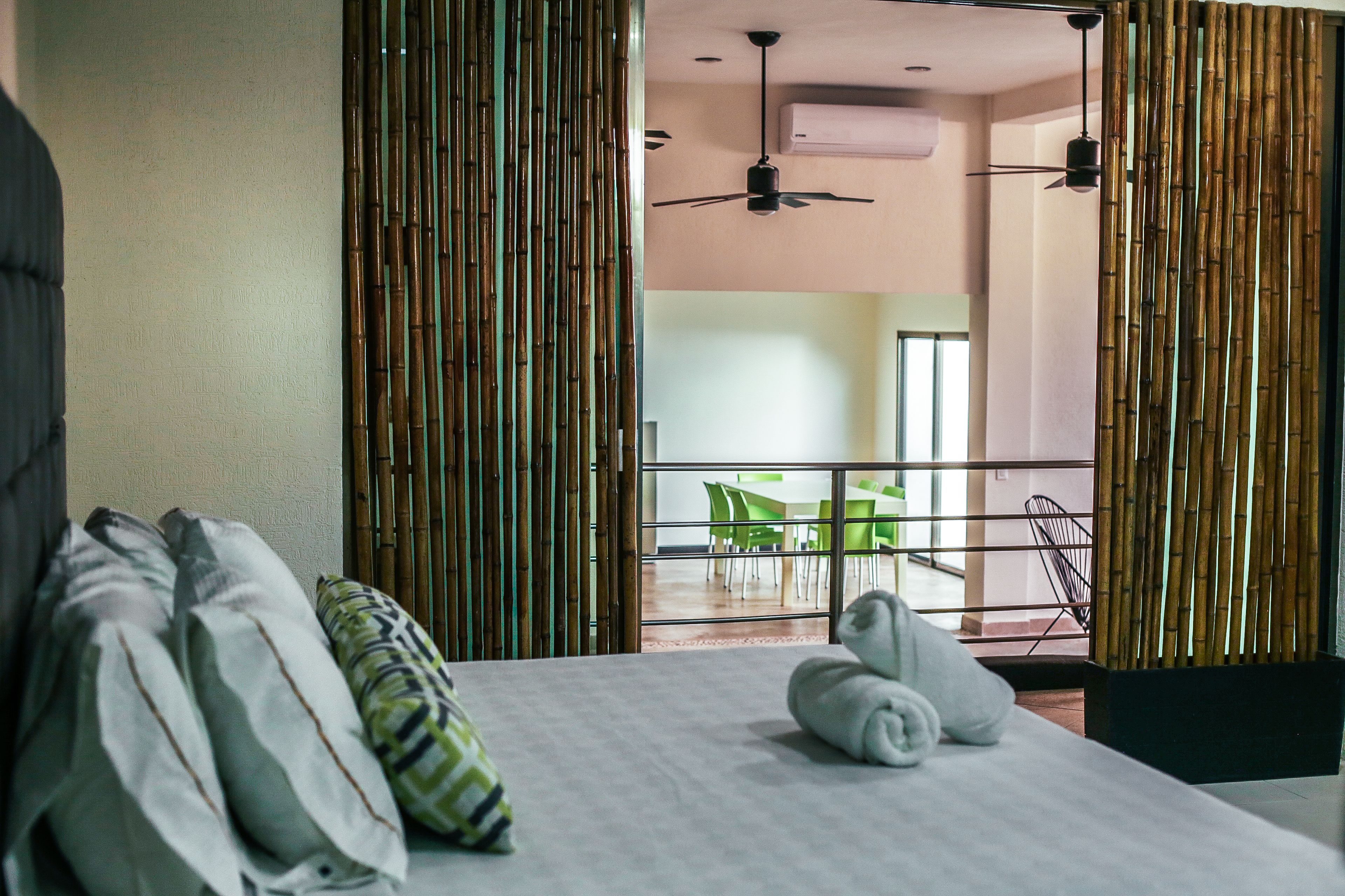 Habitación de hotel con cama, almohadas, una toalla doblada y vista a un comedor con sillas y mesa.