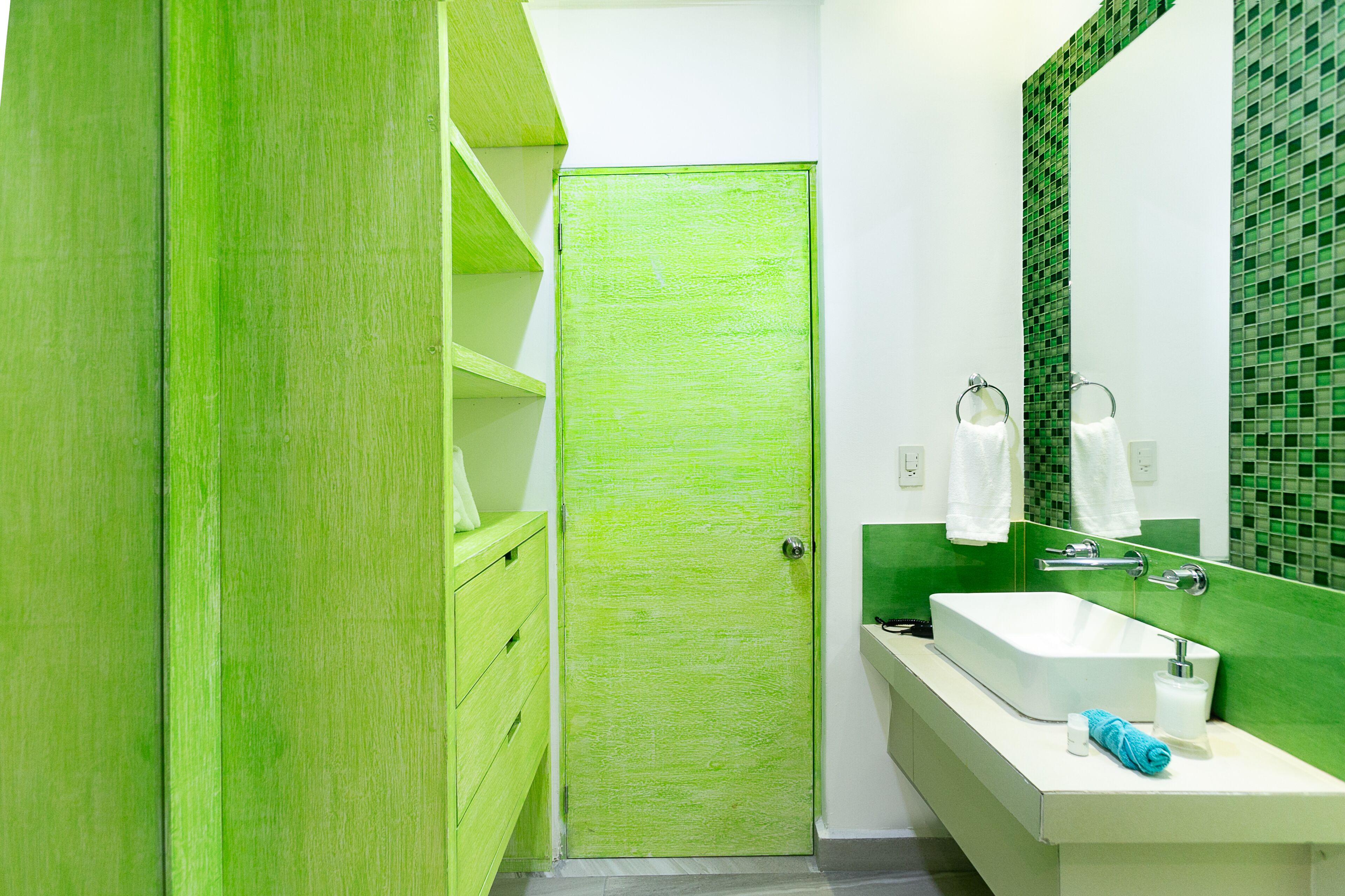 A bathroom with a green door, white sink, and green tiled backsplash.