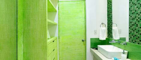 Un bagno con una porta verde, un lavandino bianco e uno schienale piastrellato in verde.