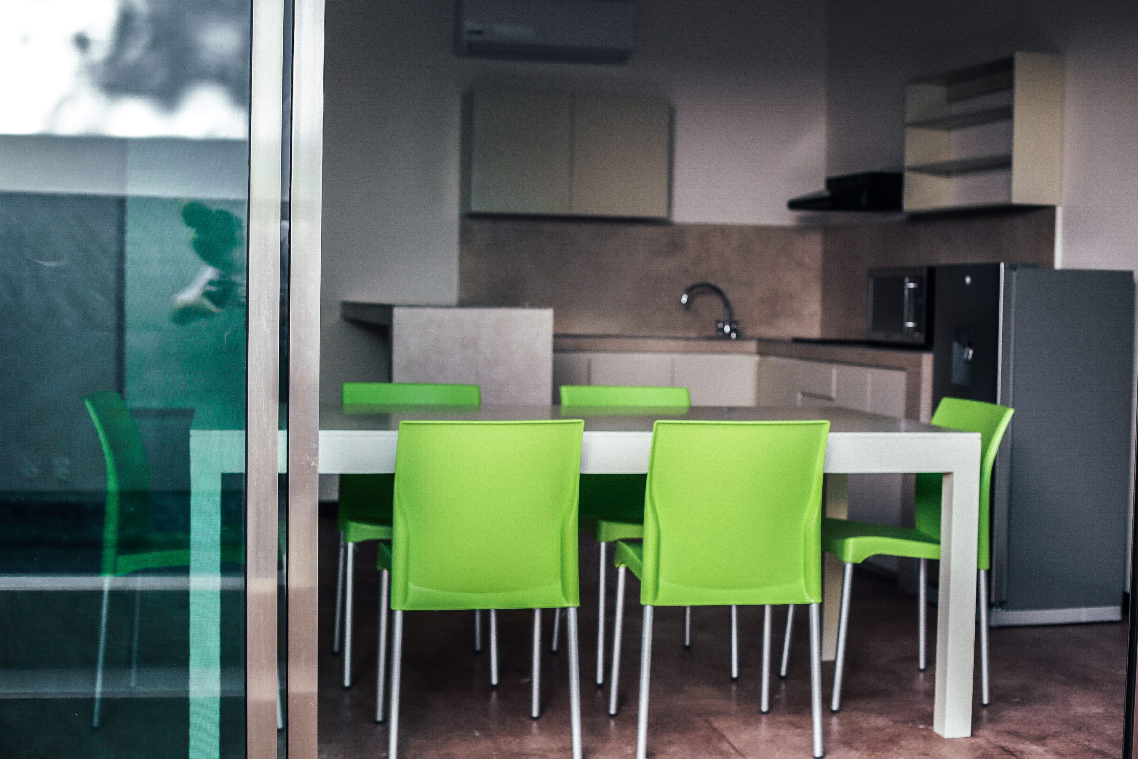 Una cocina moderna con encimera blanca, sillas verdes y un refrigerador de acero inoxidable.