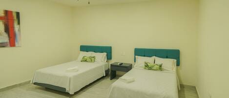 A hotel room with two beds, each with a teal headboard, white bedding, and a remote control on the nightstand.